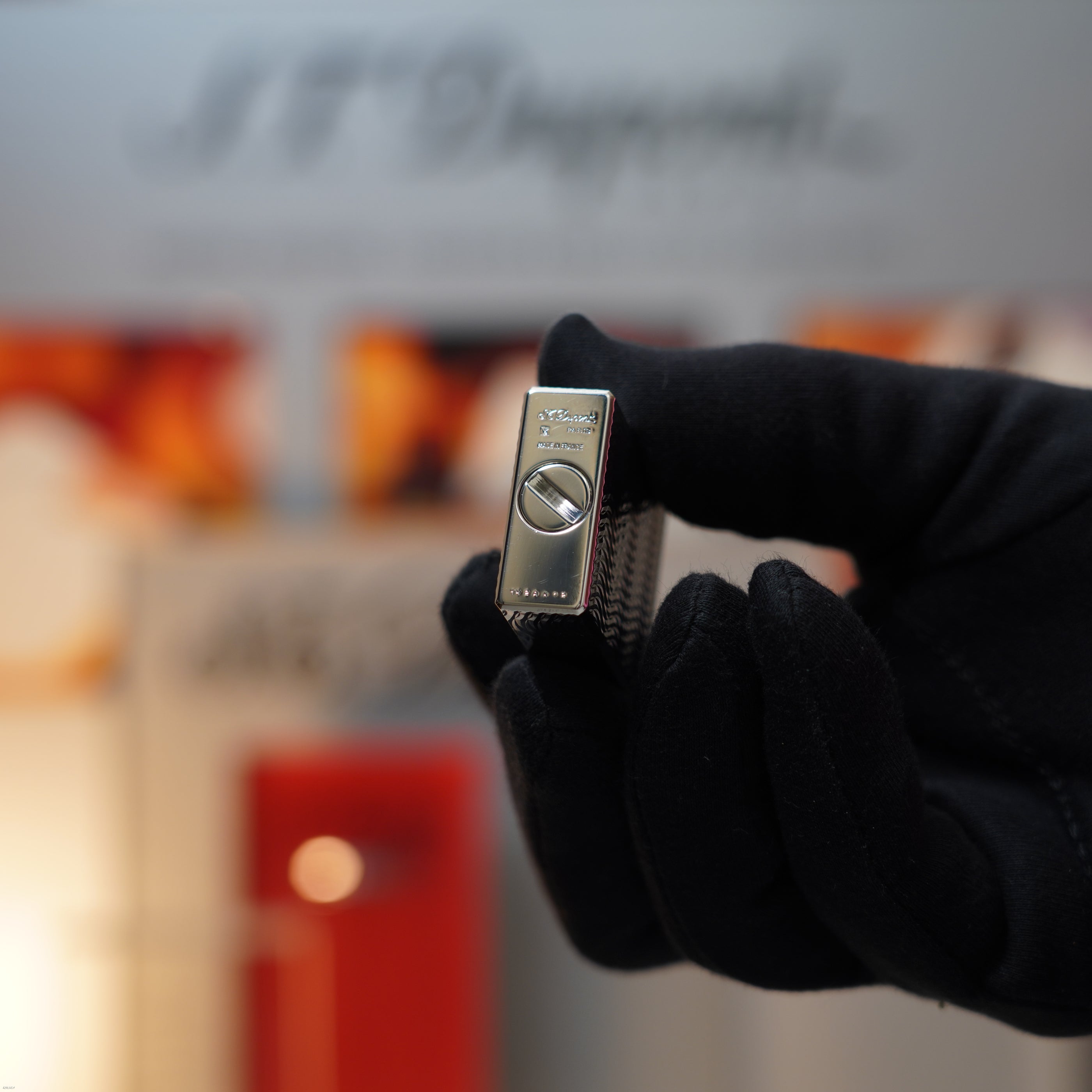 A gloved hand holds a Vintage 1990 Lucy Lighter Ligne 1 Small Size Rare 3D Wave Pattern Heavy Silver Finish Lighter, displaying the brand name and distinctive design against a blurred background.