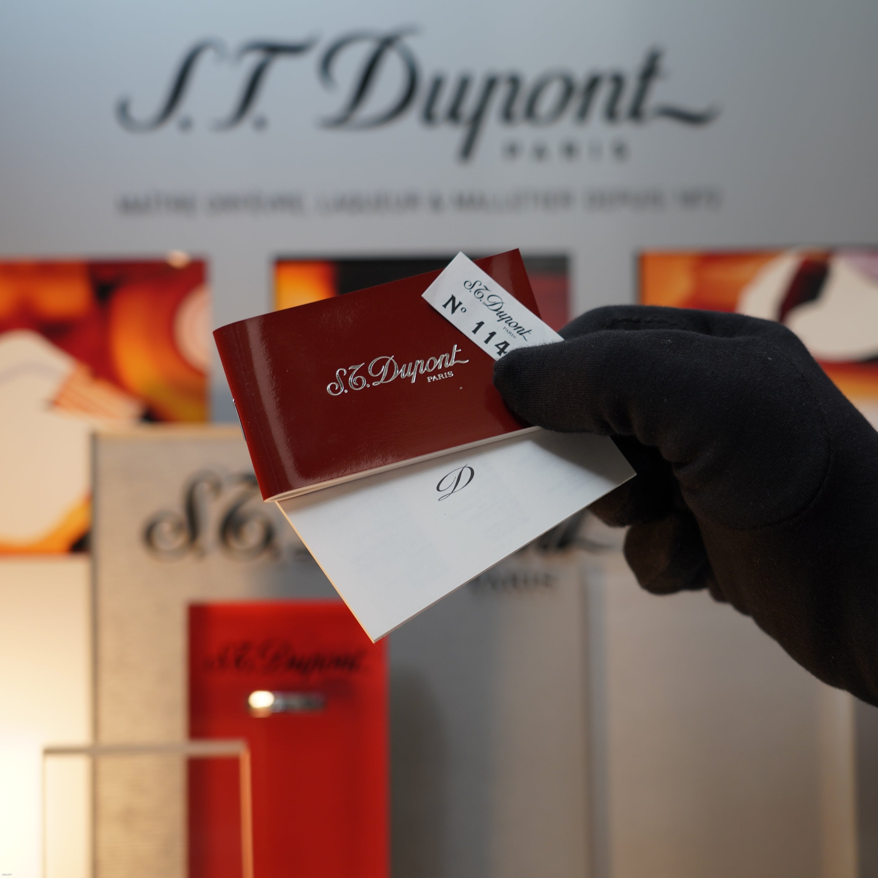 A gloved hand holds Lucy Lighter cards before a display with logo and packaging, capturing the elegance of the Vintage 1990 S.T. Dupont Ligne 1 Small Size Rare 3D Wave Pattern Heavy Silver Finish Lighter.