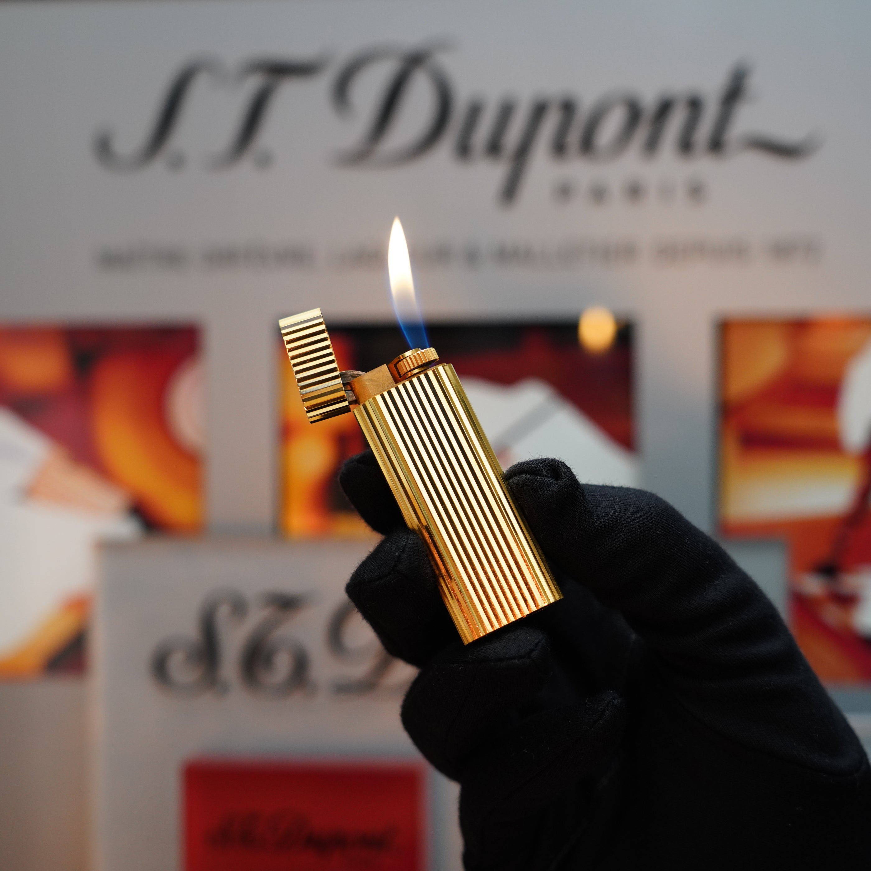 A gloved hand holds a lit gold striped lighter in front of a blurred Cartier Paris sign, evoking the elegance of the Le Must Series with its luxurious 24k Gold Finish on the Vintage 1980 Cartier Vertical Line Lighter.