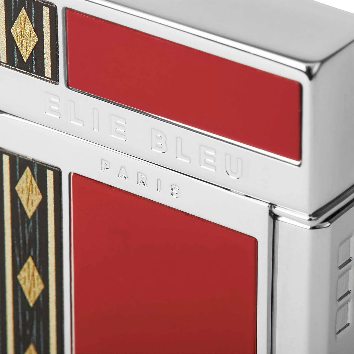 Close-up of a metallic silver lighter with bold red enamel panels and black-and-gold geometric accents. The brand name 'ELIE BLEU' is embossed on the silver metal, with 'PARIS' below it.