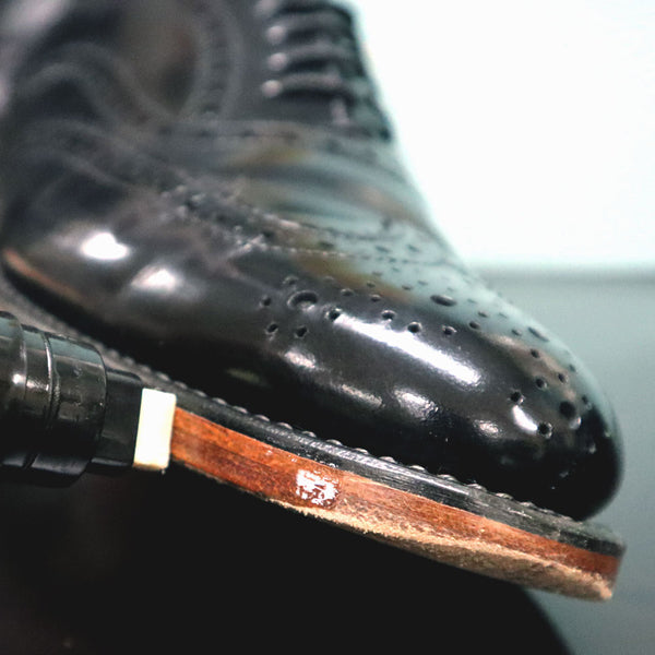 Close-up of a black leather shoe with a wooden sole and a brush on a blurred background