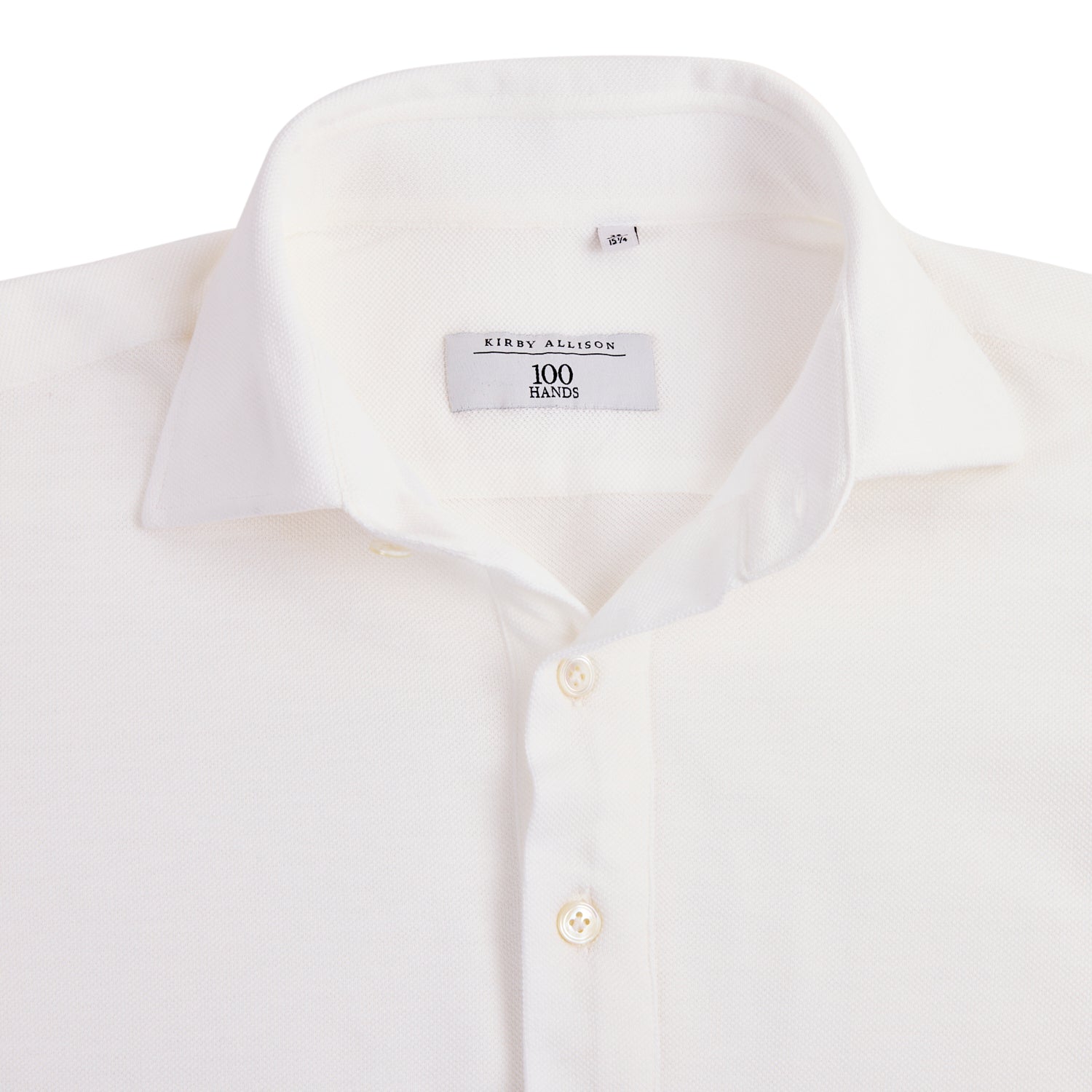 A close-up of a white long sleeve knit polo featuring a classic collar and white buttons, with a label inside that reads "Kirby Allison x 100Hands," crafted from the finest Cacciopoli jersey yarns.