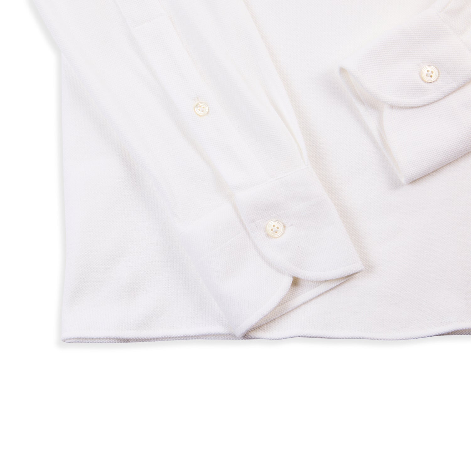 Close-up of a 100 Hands x Kirby Allison White Long Sleeve Knit Polo lying on a flat surface, showcasing the cuffs, buttons, and part of the front. This shirt is part of the exclusive collection available from KirbyAllison.com, crafted with premium Cacciopoli jersey yarns.