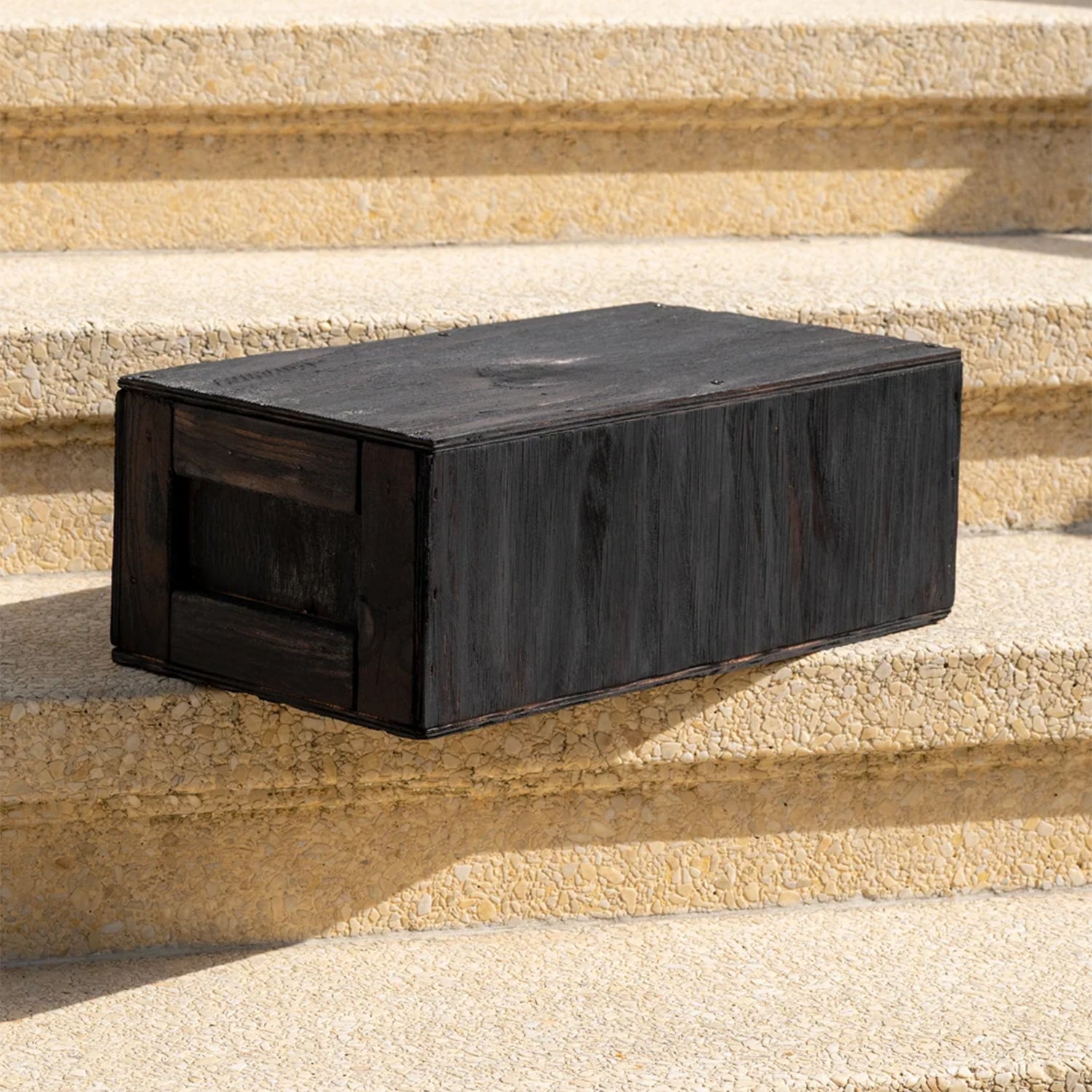 A rectangular dark wooden crate, resting on outdoor concrete steps.
