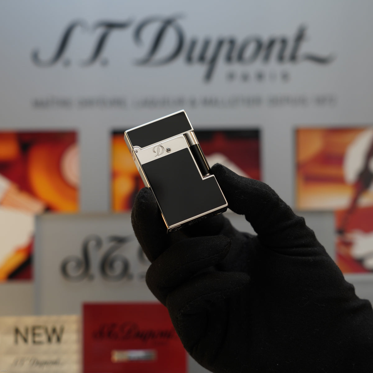 S.T. Dupont black lacquer lighter with platinum band held in gloved hand against branded packaging.