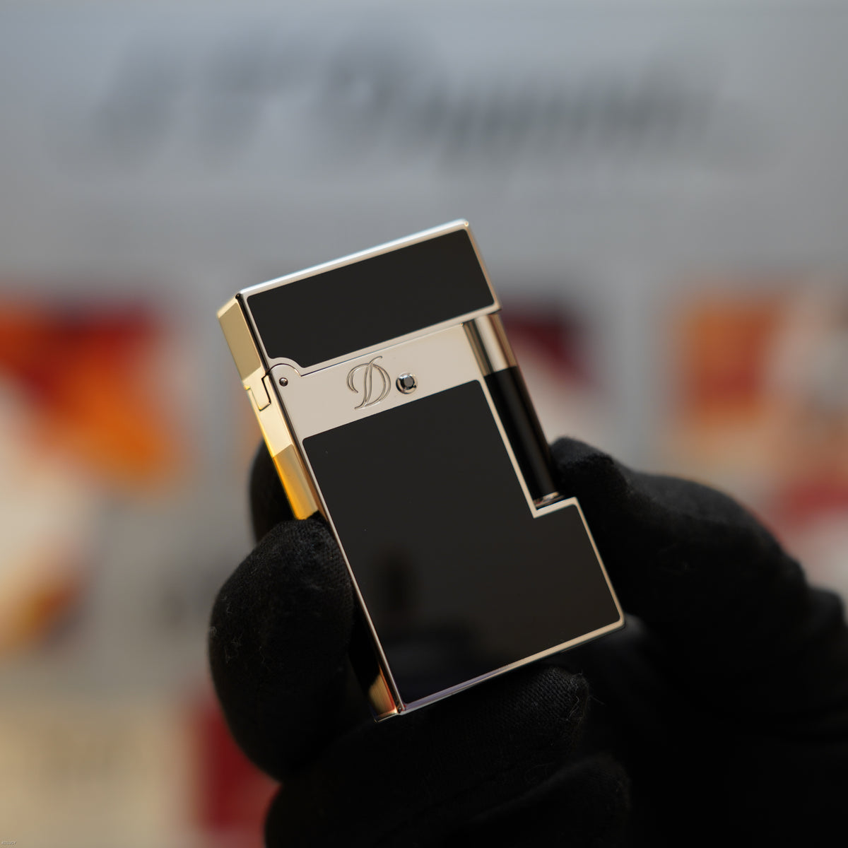 S.T. Dupont Ligne 2 lighter with black lacquer body, platinum-tone band with logo, and gold-toned trim held in a gloved hand.