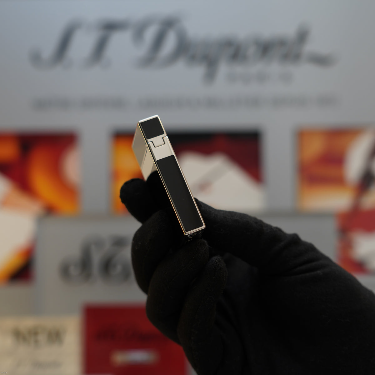 Black and platinum rectangular lighter with polished metal top held in gloved hand.