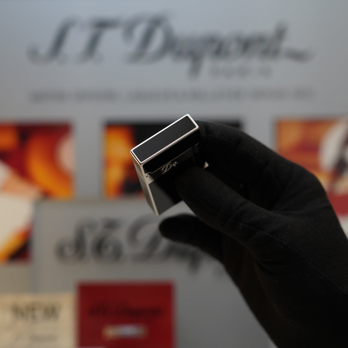 Black rectangular lighter with platinum trim held in hand, displaying engraved detail on top surface.