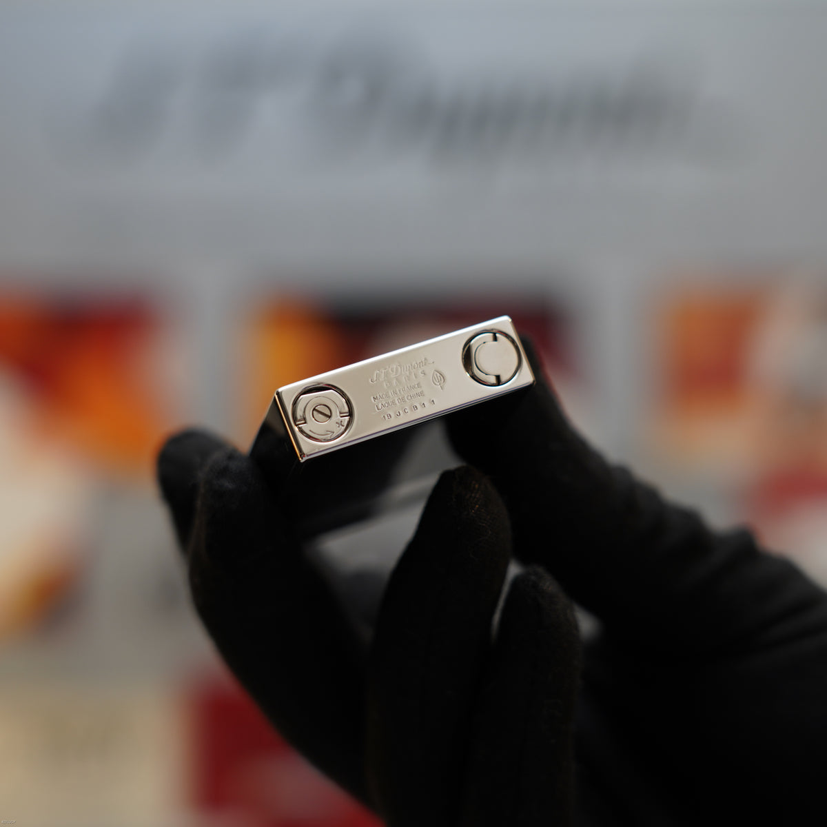 S.T. Dupont Ligne 2 lighter with platinum top plate and black body held in gloved hand.