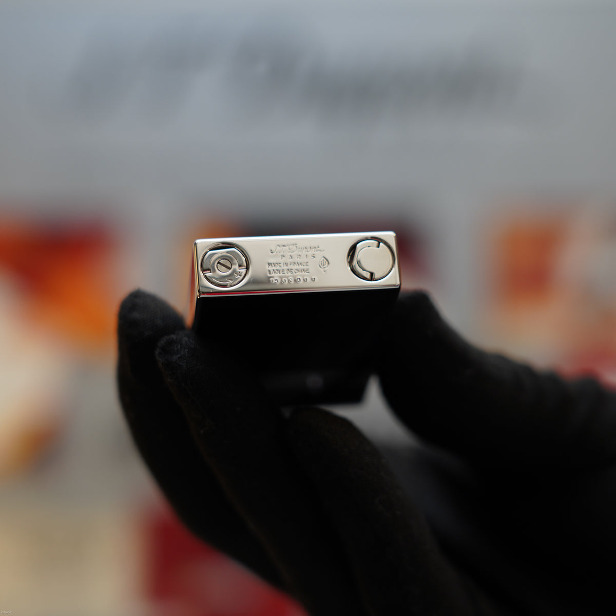 S.T. Dupont Ligne 2 lighter with black lacquer body and platinum-colored top held in a gloved hand.