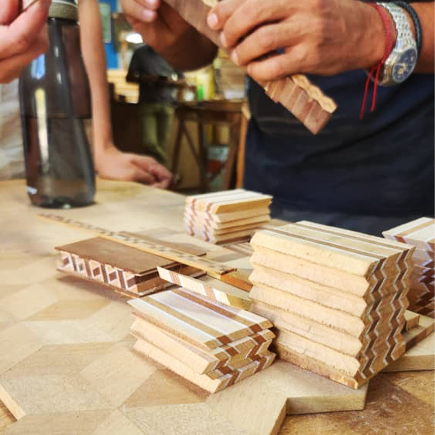 Wooden blocks with wavy patterns on a wooden surface, with people working in the background.