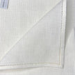 White linen pocket square with hemstitched edges and brand label visible.