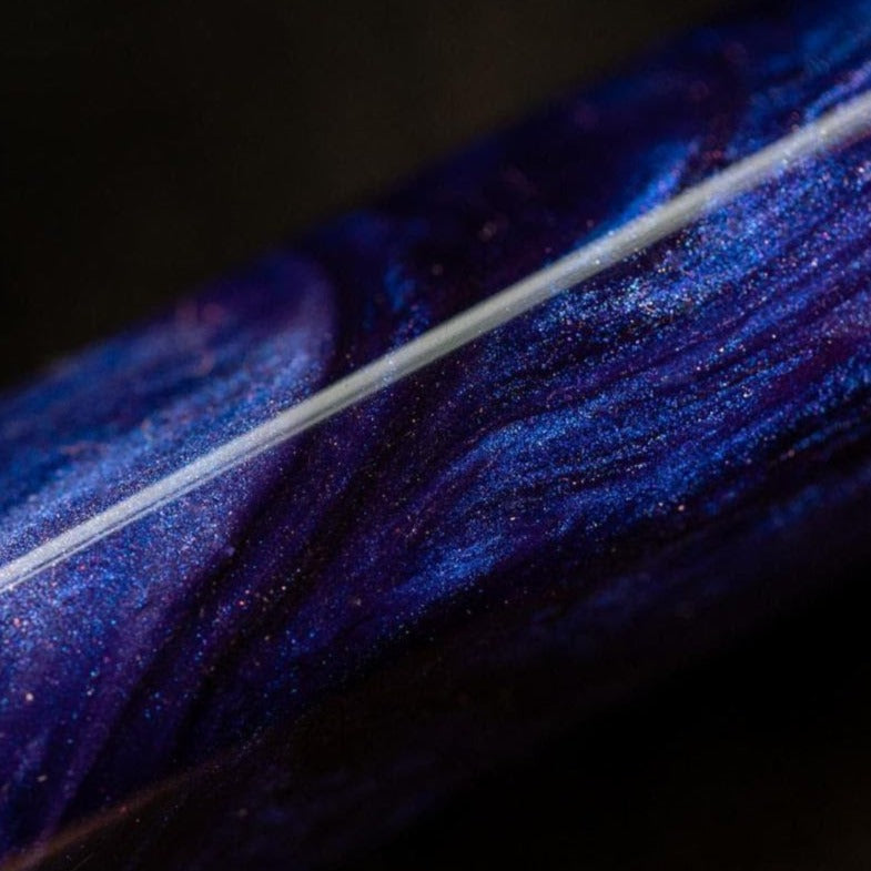 Close-up of a metallic object with swirling purple and blue patterns, reminiscent of the luxurious Visconti Medici Viola Violet - Fountain Pen (18kt Gold Nib), viewed against a dark background.