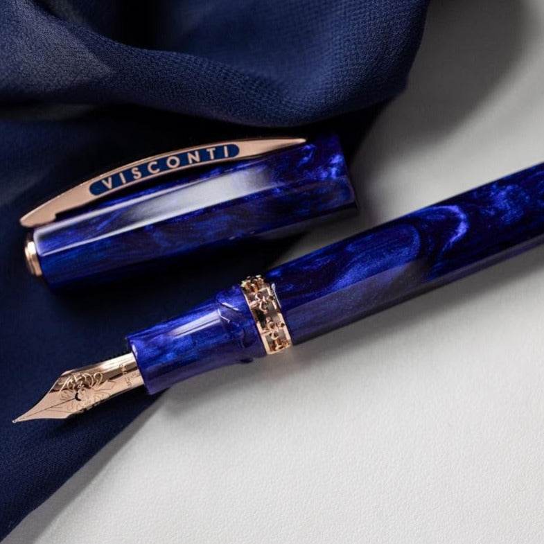 A Visconti Medici Viola Violet - Fountain Pen (18kt Gold Nib) lies open on a white surface, next to its cap and a blue cloth.