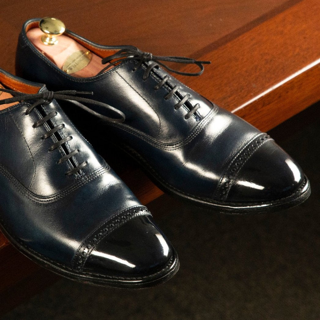 A pair of blue oxford shoes on a wooden table, showcasing the Presidential Shoe Shine Service by KirbyAllison.com.