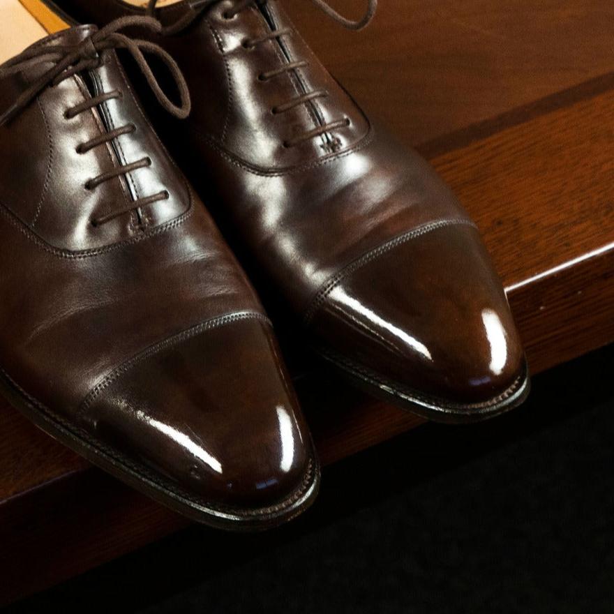 A pair of brown shoes on top of a wooden table with KirbyAllison.com's High Shine Service.