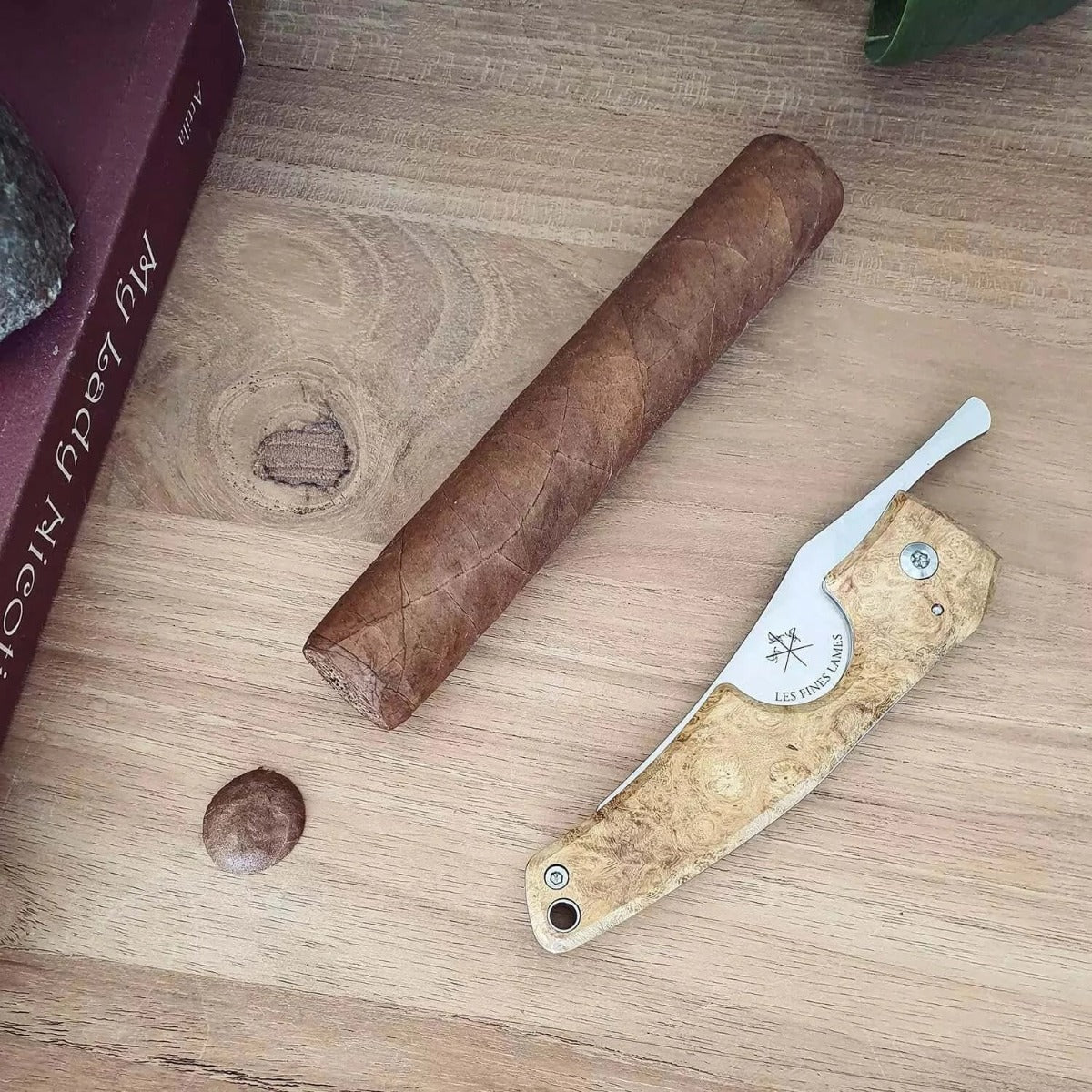 A Kirby Allison Acacia Burl Cigar Knife by KirbyAllison.com and a book on a table.