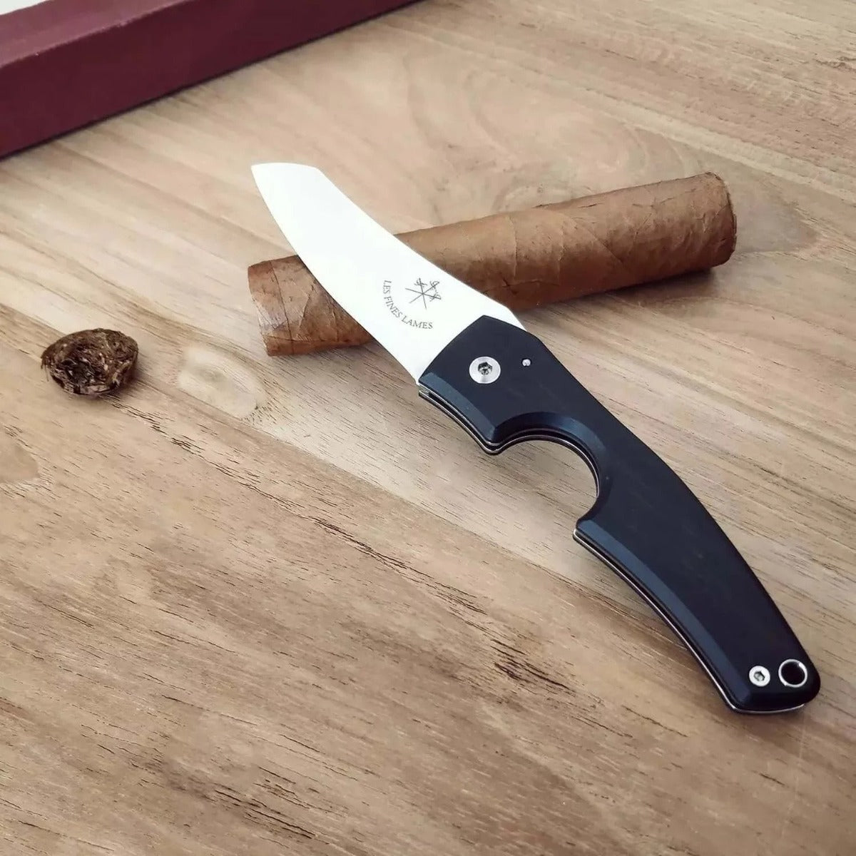 A durable Kirby Allison Ebony Wood Cigar Knife on a table next to a cigar.